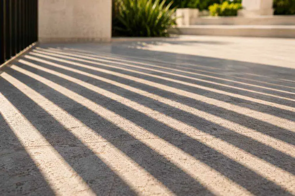 Sunlight and shadow across a paved driveway beside a gate