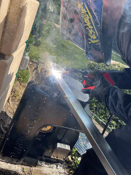 Technician welding a gate frame beside a LiftMaster opener