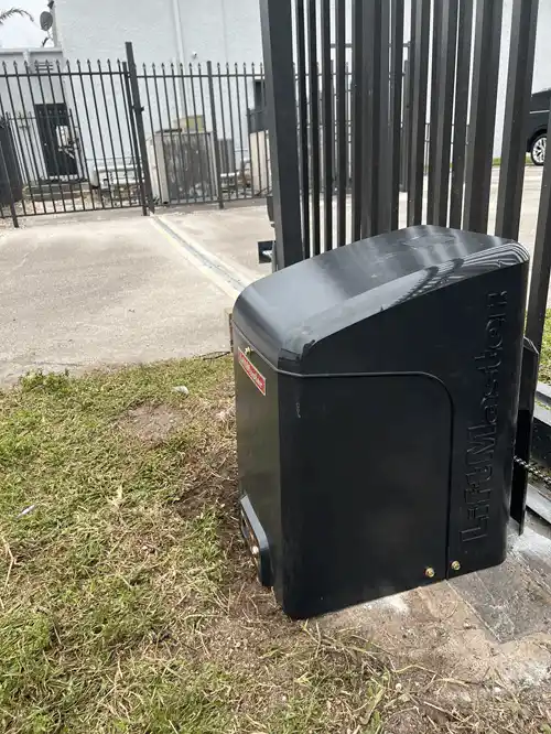 Automatic slide gate operator mounted beside a metal driveway gate